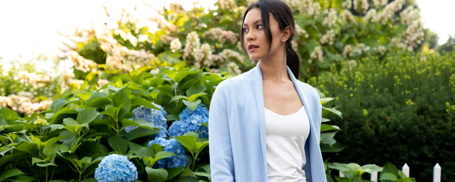 Woman wearing a light blue cashmere cardigan in a garden.